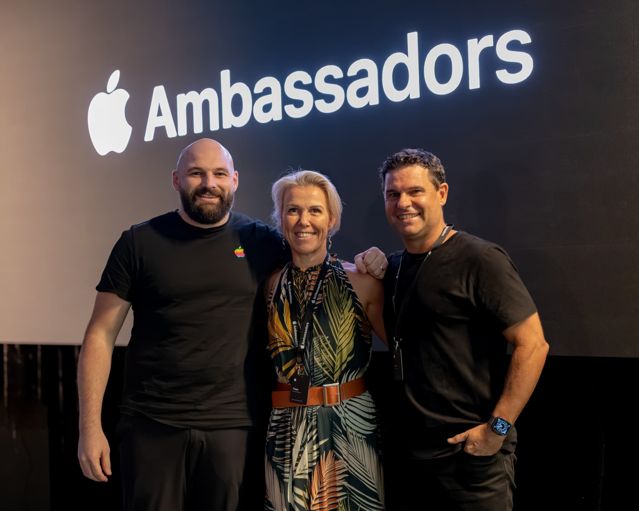 Three participants standing together in front of the Apple Ambassadors screen.