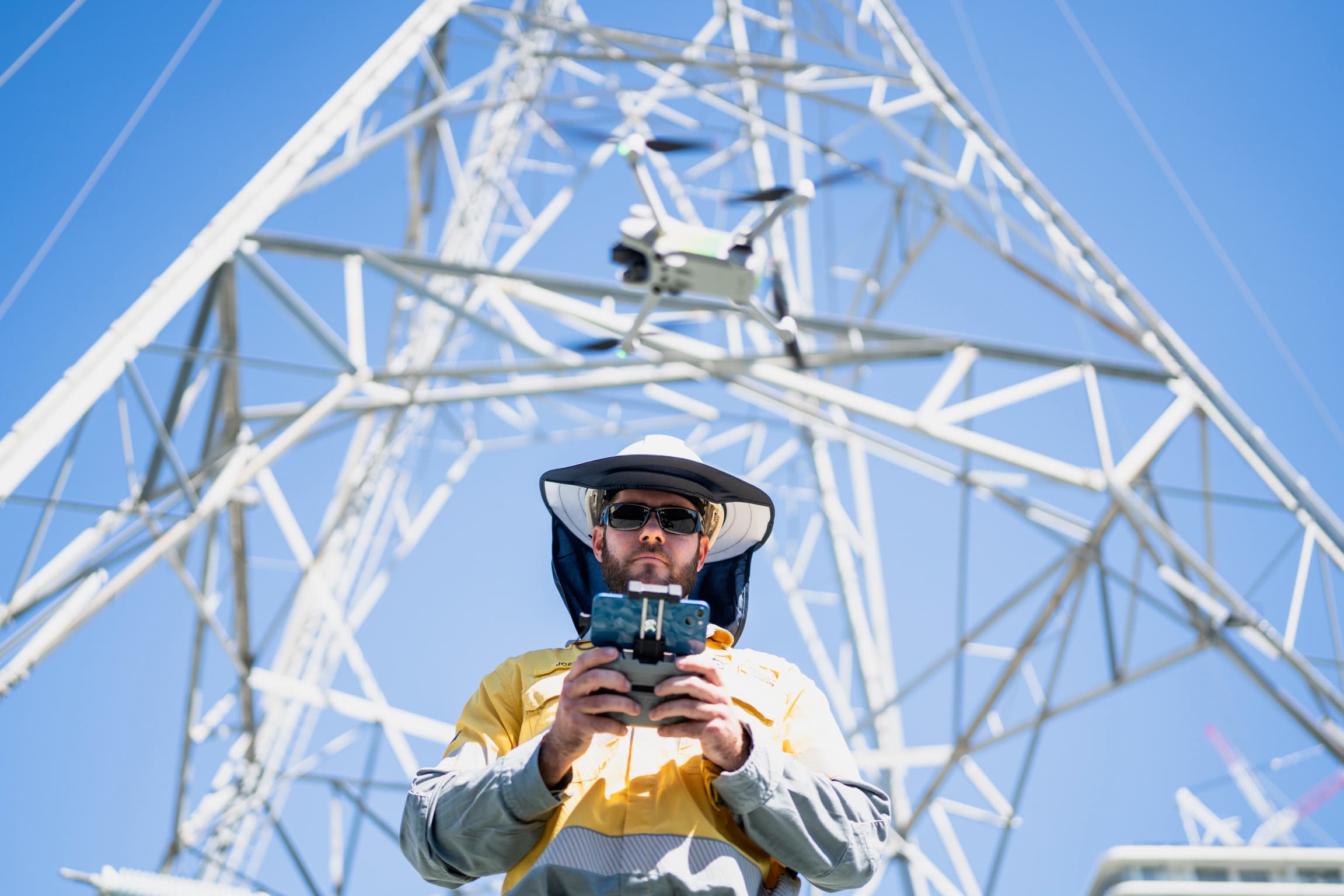 Field worker operating a drone beneath an electricity transmission tower.