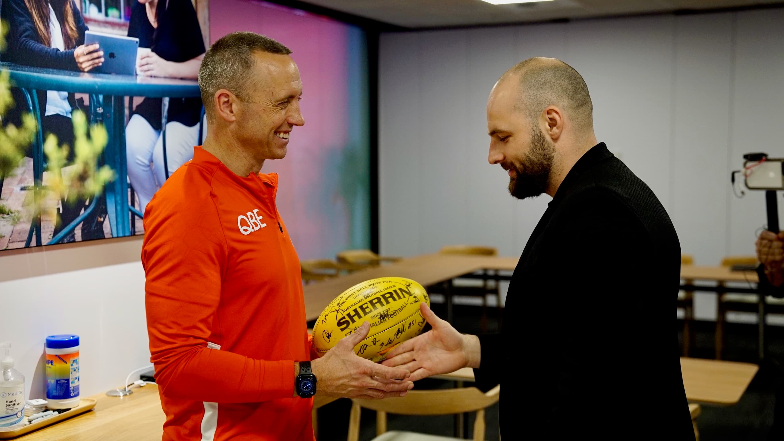 Two participants holding a signed football in The Apple Experience with Telstra workshop room.